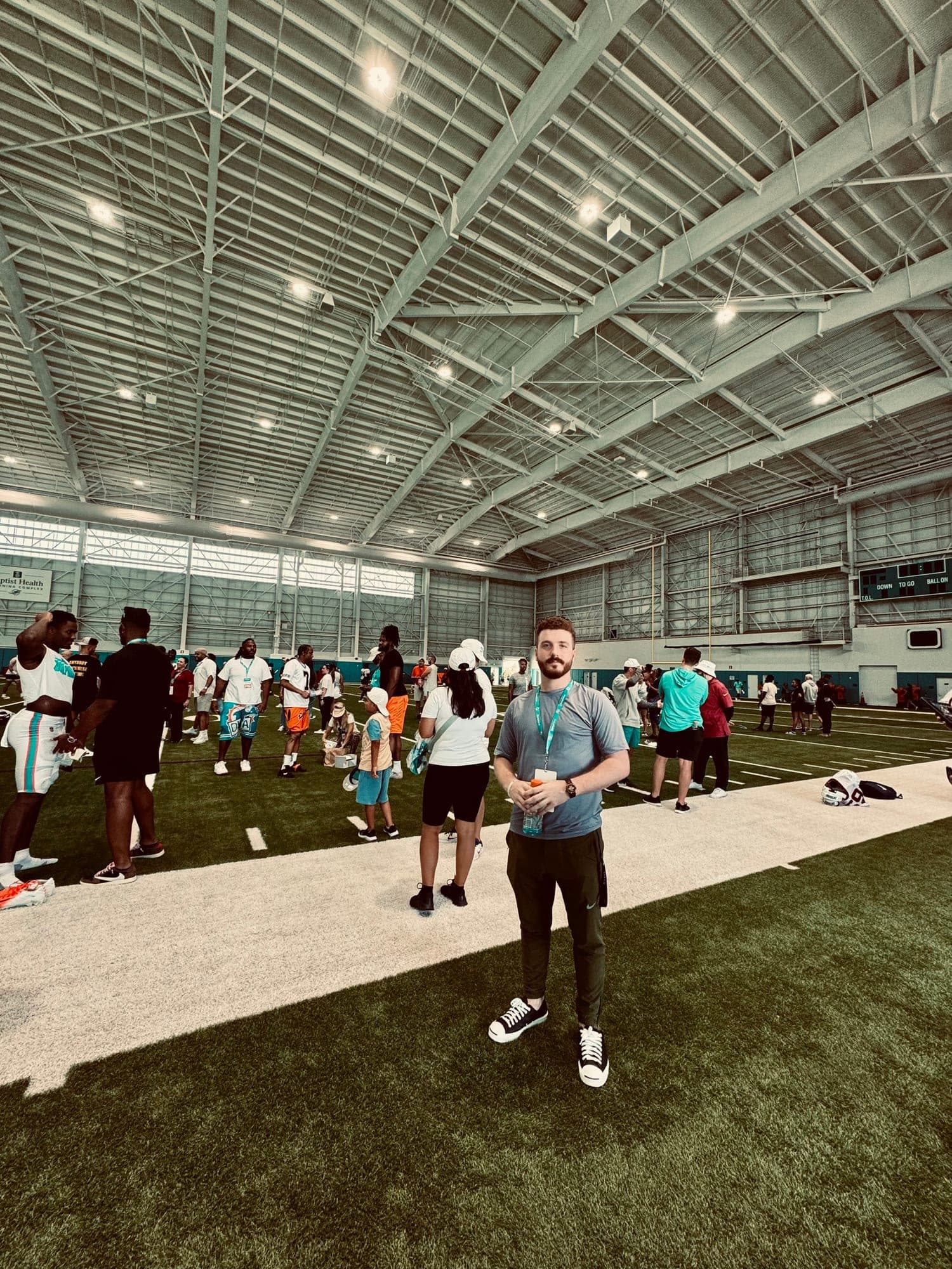 Matthew Schulster standing on an indoor practice field, with players in the background